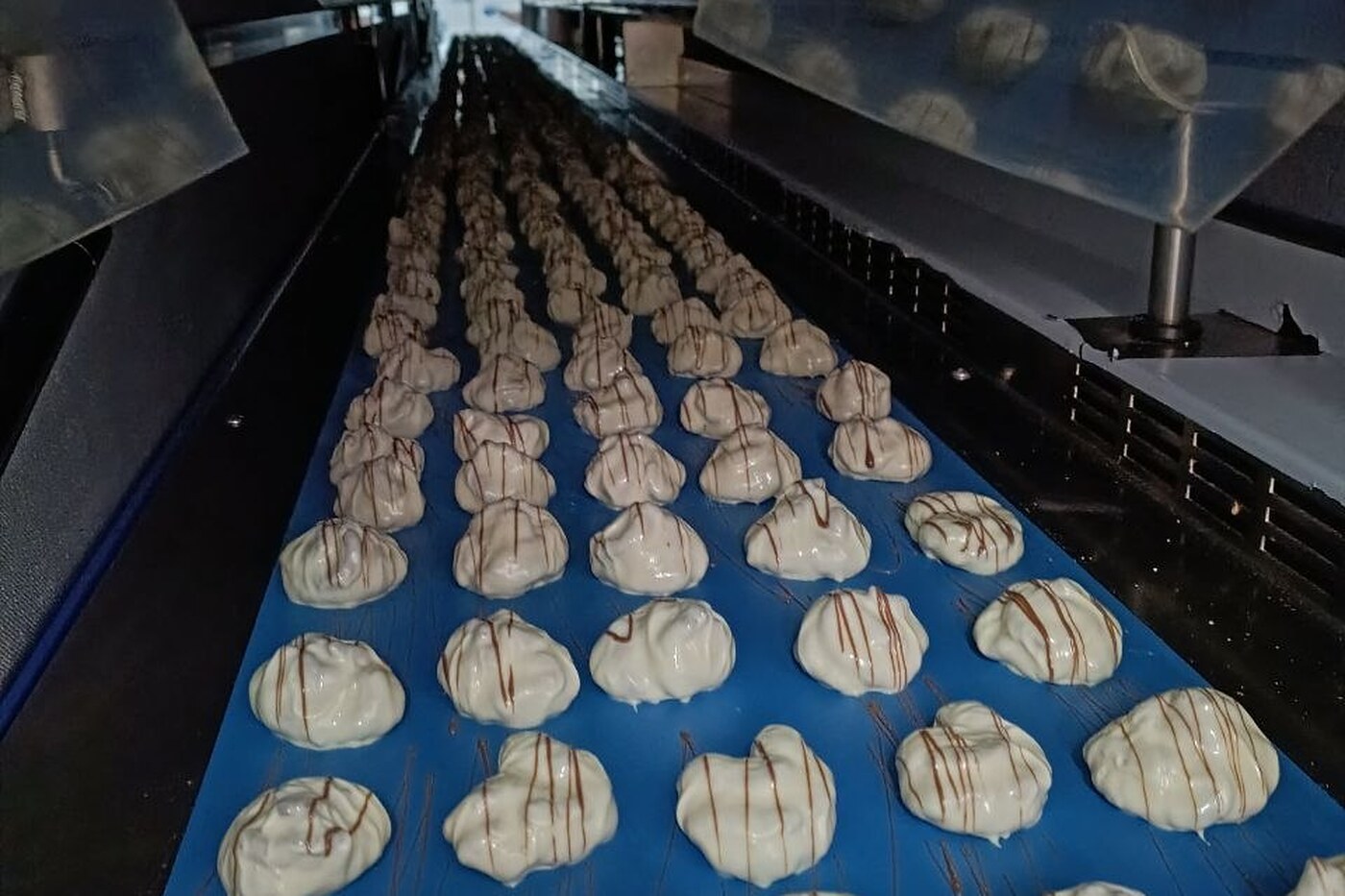 Tartuffi Bianchi on the belt inside the cooling tunnel, with the chocolate drizzle
